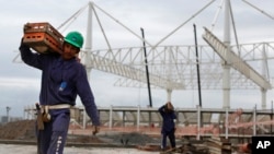 FILE - A worker carries a equipment as he walks past the aquatic stadium under construction at the Olympic Park of the 2016 Olympics in Rio de Janeiro, Brazil, March 23, 2015. 
