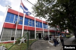 FILE - People sit outside the building which used to house a Coca-Cola bottling plant before the 1959 revolution in Havana.