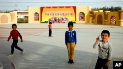 FILE - Uyghur children play at a square where a poster showing Han Chinese and Uyghurs posing together in a photograph with the words "Hotan City Unity New Village Unity Square" on display, at the Unity New Village in Hotan in western China's Xinjiang region on Sept. 20, 2018.