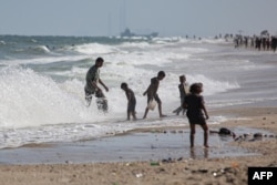 Children play on the beach as a ship that is part of international humanitarian aid efforts is moored in the background at the U.S.-built Trident Pier, in Deir el-Balah, central Gaza Strip, on May 24, 2024.