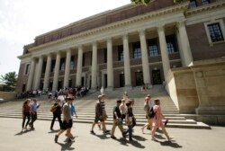 FILE - People walk past an entrance to Widener Library, behind, on the campus of Harvard University, in Cambridge, Massachusetts, July 16, 2019.