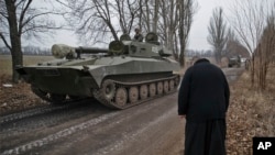 FILE - A priest bows as Russia-backed separatist fighters drive in a self propelled 152 mm artillery piece, part of a unit moved away from the front lines, in Yelenovka, near Donetsk, Ukraine, Feb. 26, 2015. 
