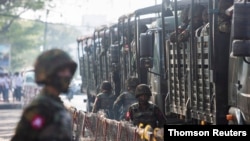 Soldiers stand next to military vehicles as people gather to protest against the military coup, in Yangon on June 2021.