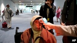Seorang petugas memeriksa temperatur seorang penumpang setibanya di bandara Soekarno-Hatta, Rabu (22/1). (AP Photo/Tatan Syuflana)