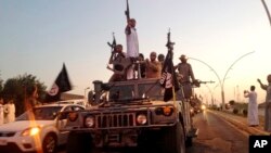 FILE - Fighters from the Islamic State group parade in a commandeered Iraqi security forces armored vehicle near the northern city of Mosul, Iraq, June 23, 2014.