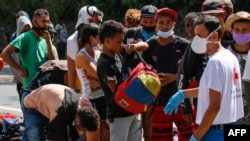 Migrantes venezolanos usan mascarilla mientras hacen cola para recibir alimentos y medicamentos de miembros de la Cruz Roja en una carretera en Cúcuta, Colombia, en la frontera con Venezuela, el 2 de febrero de 2021.