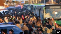 This picture released by Aleppo 24 shows residents gathered near green government buses as they hold their belongings for evacuation from eastern Aleppo, Syria, Dec. 15, 2016.
