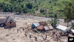 Para penyintas berjalan di antara puing-puing di samping bangunan yang hancur akibat banjir di desa Nyamukubi, provinsi Kivu Selatan, di Kongo, Senin, 8 Mei 2023.(AP/Justin Kabumba)