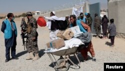 FILE - A local aid worker from pushes a wheelbarrow loaded with aid supplies outside a distribution center as a Taliban fighter secures the area, on the outskirts of Kabul, Afghanistan, Oct. 28, 2021.