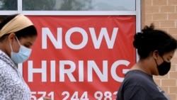 FILE - Women walk past by a 'Now Hiring' sign outside a store in Arlington, Virginia.