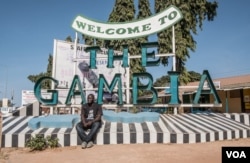 Sheriff Junior at a “Welcome to The Gambia” sign in Banjul.