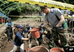 Bob Wood, Garden Valley, Calif., a members of the JPAC, Joint POW/MIA Accounting Command, second from left, deliveries a basket containing earth to South Korean Army soldiers Lee Byung-jin as he digs to search for remains of U.S. soldiers killed during the Korean War.