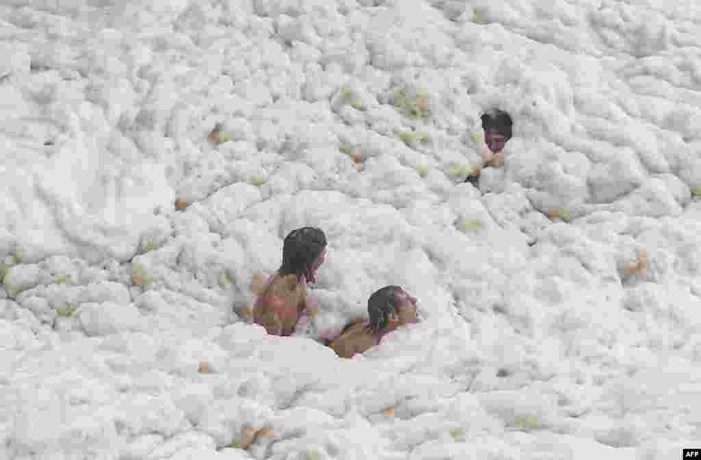 Young men play in sea foam caused by record-breaking waves as the outer fringe of Tropical Cyclone Alfred started whipping eastern Australia, in Coolangatta.