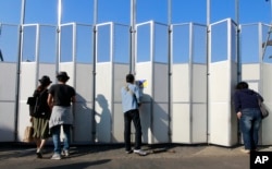 FILE - People peep in the site of the new national stadium, which will host the opening and closing ceremonies and track and field of the 2020 Tokyo Olympics, in Tokyo, Oct. 2, 2016.