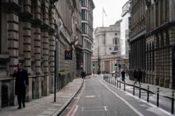 Seorang pria berbicara di telepon sambil berjalan di jalan kosong di distrik keuangan, yang dikenal sebagai The City, di London, Senin, 13 Desember 2021. (Foto: AP)