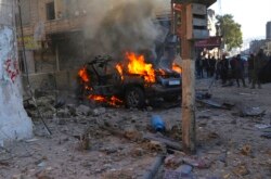 Syrians gather around a burning car hit by a shell, in the town of Afrin, north of Aleppo, Jan. 20, 2022, in this photo provided by the Syrian Civil Defense White Helmets.