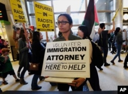 A woman offers legal services at the customs arrival area as demonstrators opposed to President Donald Trump's executive orders barring entry to the U.S. by Muslims from certain countries march behind at the Tom Bradley International Terminal at Los Angel