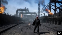 FILE - A worker carries a metal rod at the frontline Avdiivka coking plant in eastern Ukraine, Aug. 4, 2015.