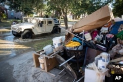 A military vehicle passes flood-damaged belongings piled on a homeowners' front lawn in the aftermath of Hurricane Harvey at the Canyon Gate community in Katy, Texas, Sept. 7, 2017.