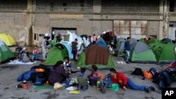 Refugees and migrants sit outside their tents at the Athens' port of Piraeus, March 10, 2016.