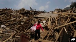 FILE - A woman carries salvaged goods through rubble following a massive earthquake in Longtoushan, in southwest China's Yunnan province, Aug. 6, 2014. A magnitude 6.1 quake struck May 20, 2021, in the province, killing at least two people. 