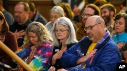 Planned Parenthood official Vicki Cowart, center, joins others in putting their hands on their hearts at All Souls Unitarian Universalist Church in Colorado Springs, Colo., during a vigil for victims of Friday's shooting at a Planned Parenthood clinic, Nov. 28, 2015.