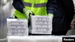 Pfizer employees handle containers of vaccine as U.S. President Joe Biden tours a Pfizer manufacturing plant producing the coronavirus vaccine in Kalamazoo, Michigan, Feb. 19, 2021. 