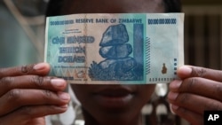 FILE - A woman holds a 100 trillion-dollar note in Harare, the highest denomination printed by the Reserve Bank of Zimbabwe. 