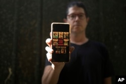 Yuval Haran, whose family is celebrating the return of his mother, his sister and four others from Hamas captivity in Gaza, poses for a portrait with a picture on his phone of his family's hostage posters, in Herziliya, Israel, on Dec. 4, 2023.