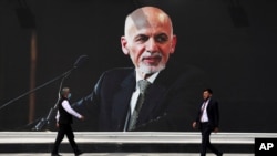 People walk near a mural of President Ashraf Ghani at Hamid Karzai International Airport, in Kabul, Afghanistan, Aug. 14, 2021.