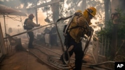 Firefighters pull hoses and spray flames behind a home in the Pacific Palisades area of Los Angeles, Oct. 21, 2019. Santa Ana winds are in the weekend forecast for Southern California, prompting another power blackout.