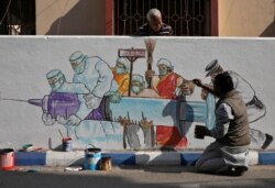 FILE - A man applies finishing touches to graffiti representing a vaccine, amidst the spread of coronavirus disease, in Kolkata, India, Jan. 2, 2021.