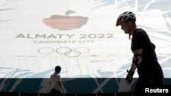 People walk past a banner promoting Almaty candidate city for 2022 Winter Olympic Games at the Medeu skating oval in Almaty, Kazakhstan, July 26, 2015.