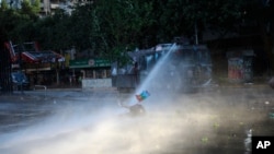 An anti-government protester, holding a Mapuche flag, is brought down by the jet spray of a police water cannon, in Santiago, Chile, Oct. 31, 2019.