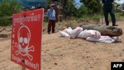 រូបឯកសារ៖ សមាជិក​មជ្ឈ​មណ្ឌល​សកម្ម​ភាព​កម្ចាត់​មីន​កម្ពុជា​(CMAC) (ឆ្វេង) និង​ប៉ូលិស​ឈរ​យាម​ពី​ក្រោយ​គ្រាប់​បែក​ម៉ាក ៨២ នៅ​ខេត្ត​កណ្ដាល កាលពី​ថ្ងៃ​ទី​២១ ខែ​ឧសភា ឆ្នាំ​២០១៥។