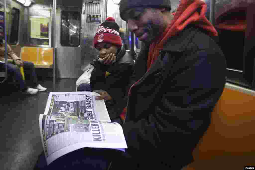 Daniel Mitchell talks with his son Daniel Mitchell 2nd about the death of two police officers who were fatally shot in the Brooklyn borough, as they read a local paper on the G train in New York, Dec. 22, 2014.