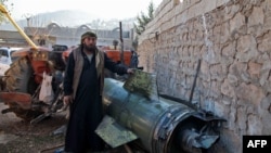 FILE - A man stands next to a fragment of a ground-to-ground missile fired by government forces that hit a makeshift camp in the village of Qah near the Turkish border in northwestern Idlib province, Nov. 21, 2019.