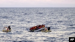 FILE - Photo provided by the Italian Navy shows rescue crews approaching migrants on a rubber boat some 40 miles (65 kilometers) from the Libyan capital, Tripoli.
