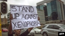 A South African holds a sign as she stands on the side od a road in Sandton, as xenophobic violence continued, on April 18, 2015. 