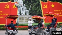 អ្នកធាក់ស៊ីក្លូរង់ចាំដឹកអតិថិជននៅមុខបដាដ៏ធំតំណាងឲ្យសមាជគណបក្ស​កុម្មុយនីស្ត​វៀតណាមលើកទី១៣ នៅទីក្រុងហាណូយ ប្រទេសវៀតណាម ថ្ងៃទី២៥ ខែមករា ឆ្នាំ២០២១។