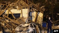 TOPSHOT - This photo taken on June 13, 2020 shows a man walking past a building and car damaged by a tanker explosion near Wenling, in China's eastern Zhejiang province. - The number of people killed in a tanker truck explosion on a highway in…