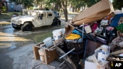 FILE - A military vehicle passes flood-damaged belongings piled on a homeowners' front lawn in the aftermath of Hurricane Harvey at the Canyon Gate community in Katy, Texas, Sept. 7, 2017.