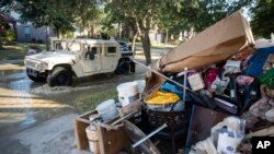 FILE - A military vehicle passes flood-damaged belongings piled on a homeowners' front lawn in the aftermath of Hurricane Harvey at the Canyon Gate community in Katy, Texas, Sept. 7, 2017.