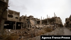 Posters of Syria's President Bashal al-Assad hang on a building in the central Syrian town of al-Qaryatain in the Homs province, Dec. 20, 2021, next to buildings damaged during fbattles in 2015 between the Islamic State group (IS) and government forces. 