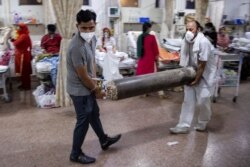 Relatives of a woman suffering from the COVID-19, carry an oxygen cylinder as she receives treatment in the emergency room of Holy Family Hospital in New Delhi, India, May 1, 2021.