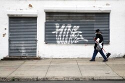A person wearing a protective face mask as a precaution against the coronavirus walks past a shuttered business in Philadelphia, April 23, 2020.