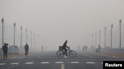 FILE - A newspaper vendor rides his bicycle on a smoggy morning in New Delhi, India, Dec. 1, 2015.