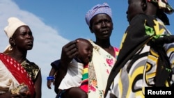 FILE - A woman carries a baby as she talks with other women talk at a food distribution center in Minkaman, Lakes State, South Sudan.
