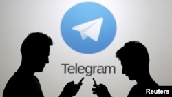 FILE - Two men pose with smartphones in front of a screen showing the Telegram logo in this picture illustration taken in Zenica, Bosnia and Herzegovina, Nov. 18, 2015.