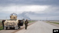 FILE - Smoke billows in the background as Kurdish peshmerga fighters take positions on the side of a road in the northern Iraqi city of Kirkuk, Jan. 30, 2015.